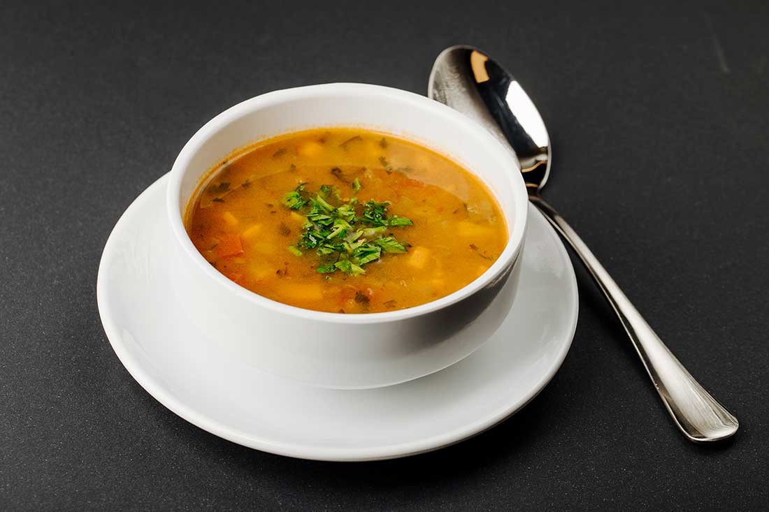 colher de sopa, um dos tipos de talheres usados em refeições, ao lado de um prato fundo com sopa em um cenário escuro