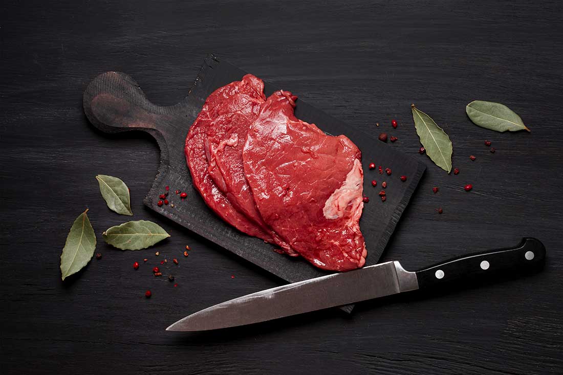 faca para carnes, um dos tipos de talheres usados em refeições, ao lado de um pedaço de carne crua em uma tábua
