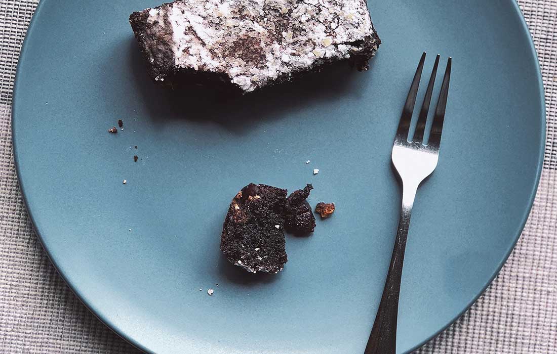 garfo de sobremesa em um prato azul com um pedaço de bolo de chocolate